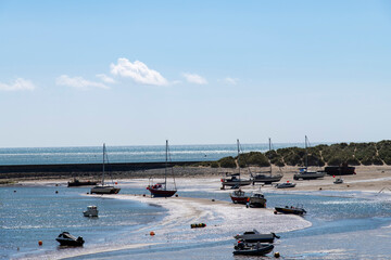 Panoramic view of the harbor of Barmouth, UK during low tide with boats on the sandbanks of the Mawddach Estuary and Afon Mawddach river against a white clouded blue sky