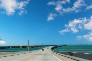 Naklejka premium Drivers’ perspective over the Seven Mile Bridge or Florida State Road A1A towards Key West, FL, USA and cars on the road with on left side the Old Seven Mile Bridge