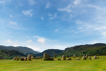 Obraz premium English Heritage Castlerigg Stone Circle of 5000 years old near Keswick, UK in the Lake District National Park on a hill overlooking surrouning hills and mountains against a white clouded blue sky