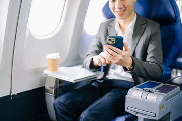 Young Asian executive excels in first class, multitasking with digital tablet, laptop and...