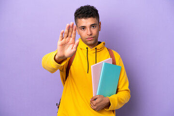 Young student Brazilian man isolated on purple background making stop gesture