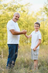 Fototapeta premium Happy weekend concept. happy grandfather and grandson are walking in the park
