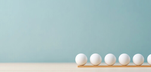 Minimalist composition of white spheres on wooden tray against light blue background, showcasing simplicity and balance.
