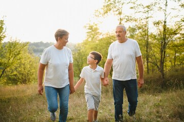 Fototapeta premium Grandparents walking with they grandson in summer sunset