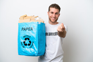 Young caucasian man holding a recycling bag full of paper to recycle isolated on white background making money gesture