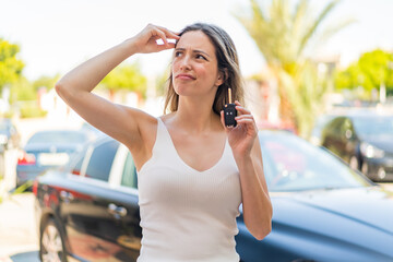 Young pretty woman holding car keys at outdoors having doubts and with confuse face expression