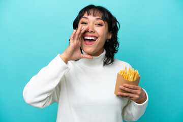 Young Argentinian woman holding fried chips isolated on blue background shouting with mouth wide...