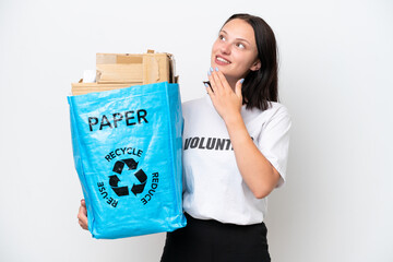 Young caucasian woman holding a recycling bag full of paper to recycle isolated on white background looking up while smiling