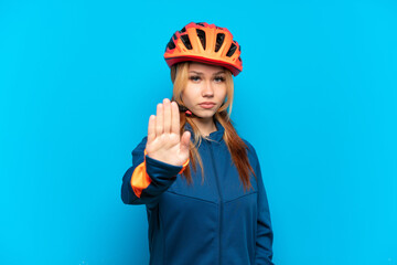 Young cyclist girl isolated on blue background making stop gesture