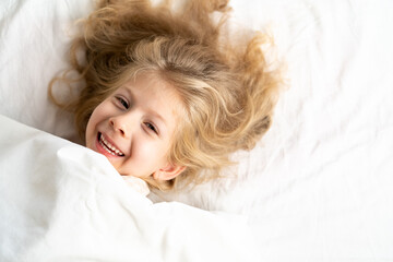 happy little girl in a white bed on a pillow, good morning, healthy baby sleep concept