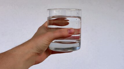 Hand holds a transparent glass with clean water. Crystal clear water in a glass held by a woman's...