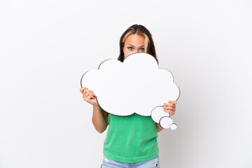 Teenager Russian girl isolated on blue background holding a thinking speech bubble and hiding behind it