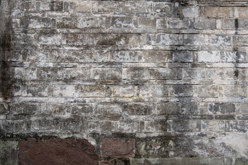 a weathered brick wall with a rough, uneven texture with signs of erosion and discoloration.Moss and lichen are growing in some of the crevices.&nbsp;a historic and timeworn surface background texture 