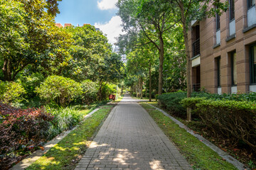 A pavement pedestrian footpath or walkway in a landscaped public garden within residential apartment blocks in a Chinese urban community, lush green trees and shrubs providing shade along walkway