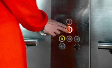 Woman in red dress pressing button inside elevator.