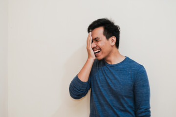 Portrait of happy Adult Southeast Asian man covers half face with palm cream background, positive emotion, copy space.