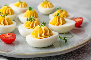 Deviled eggs with cheese, mustard and microgreens on top on a plate for Easter.