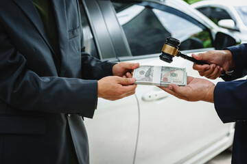 Two Asian individuals discuss a car insurance claim with an agent in front of a damaged vehicle. They review documents, discuss the policy, and address the crash and repair costs.