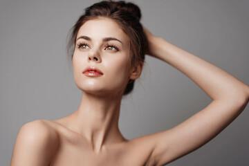 Fototapeta premium Beautiful young woman posing with her hands on her head against a gray background