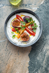 Bowl of ricotta dip with tomatoes and fig fruits, top view on a beige and grey granite background, vertical shot, copy space