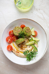 Plate with hummus, falafel and fresh vegetables, vertical shot on a beige stone background, elevated view