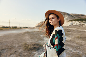 solitary woman in hat and sweater standing in desert with majestic mountains in the distance