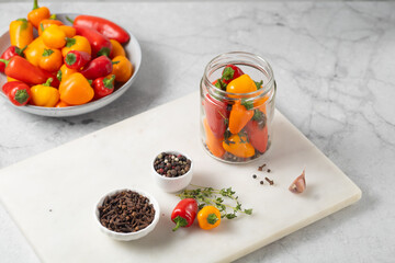 Probiotic foods. Eco friendly still life with pickled or fermented vegetables. Mini colorful bell pepper in glass jars on light grey marble background . Home food preserving or canning