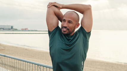 Fit guy does street workout, stretching and warming up against the sea on a cloudy day, sport motivation and sporty lifestyle