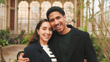 Happy young couple embracing in greenhouse, with background of arched windows and plants