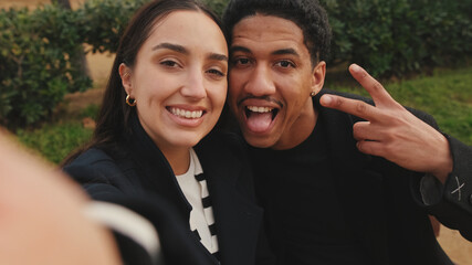 Multiracial couple taking selfie with smartphone in park, showcasing happy moments