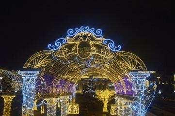 Festive Christmas illumination - bright glowing decorative arch against the night sky. New Year's city street decor.