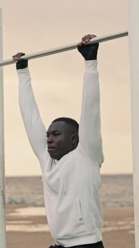 Side view of a man trains his abs and biceps outdoors on a bar, dooing l-sit pull-ups 