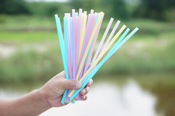 Close up hand holds colorful plastic drinking straws tubes.  Concept single use equipment for drinking, but can use for diy crafts for decoration. Reduce and recycle plastic tubes for environment.   