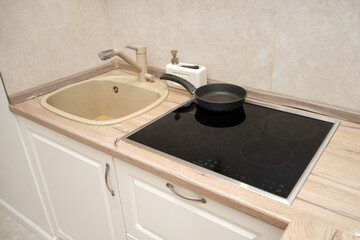 Kitchen countertop with beige sink, faucet, soap dispenser, and black frying pan on induction cooktop. Home interior concept for design and print