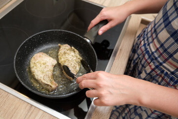 Person using tongs to flip meat slices in a frying pan on an electric stove. Close-up kitchen scene during meal preparation