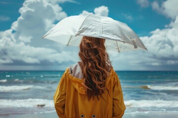 Beautiful girl holding an umbrella and wearing a stylish raincoat standing beach with back - Copy space