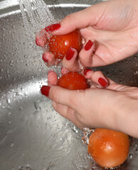Woman washing tomatoes in the kitchen sink, hands close-up. Close-up of a woman washing tomatoes in the kitchen sink. Female hands washing vegetables in the kitchen sink