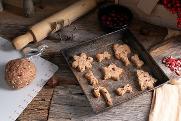 Cranberry dog cookies with a festive, rustic background with cookie cutters, rolling pin, mat, and cutting board on a wooden table.