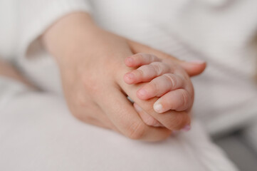 Woman mom holding newborn baby hand, close up. Mom with baby. Motherhood, family, concept of birth, connection, love and relationship with baby.