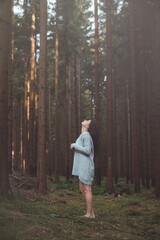 Serene woman in a cozy grey sweater stands barefoot in a tranquil forest, gazing upwards with a peaceful expression, capturing a moment of connection with nature and inner calm