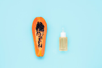 Papaya fruit and cosmetic serum bottle on light blue background. Top view, flat lay