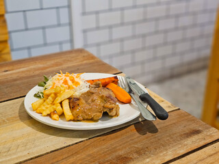 Black pepper pork steak is a thick cut of pork, grilled or fried with a rich black pepper sauce, served with French fries and fresh green vegetables on the side.