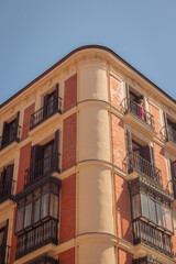 Obraz premium Tall facade of urban building in Madrid city red brick rounded architecture with black balcony sunny day blue sky