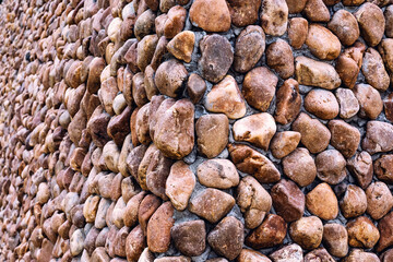 Large natural pebbles arranged to decorate beautiful and strong wall. Yellow and brown pebble stone wall. Surface and Texture background of round stone wall to use as wallpaper. lot of natural stone.