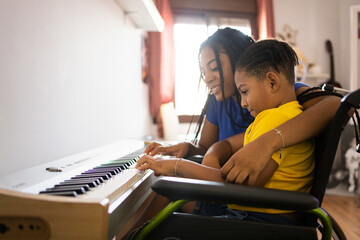 Two dark-skinned brothers play an electronic piano in their living room. The older sister hugs the little one as they play. Concept of young African people playing a piano.