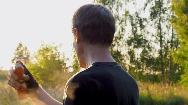 A caucasian man sprays his neck and head with mosquito repellent outdoors on a summer evening.