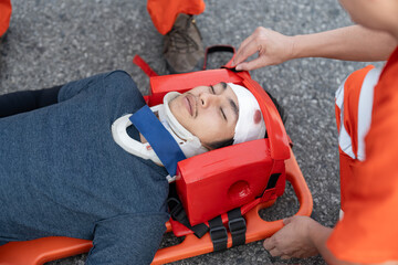Close-up of a young man with a head injury, wearing a neck brace, secured on a stretcher. EMS paramedics or emergency medical technicians performing first aid to patient.