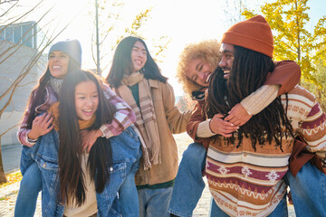 Group of five happy friends piggyback and laughing out loud outdoor, sharing good and positive mood.