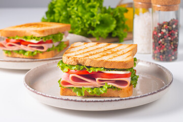 Close-up of two sandwiches with bacon, salami, prosciutto and fresh vegetables on rustic wooden cutting board. Club sandwich concept