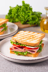 Close-up of two sandwiches with bacon, salami, prosciutto and fresh vegetables on rustic wooden cutting board. Club sandwich concept